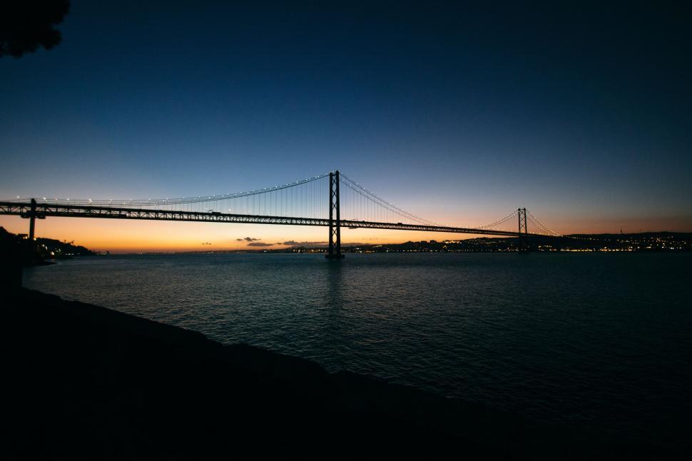 Free Image of Panoramic view of bridge over water at twilight, illuminated 