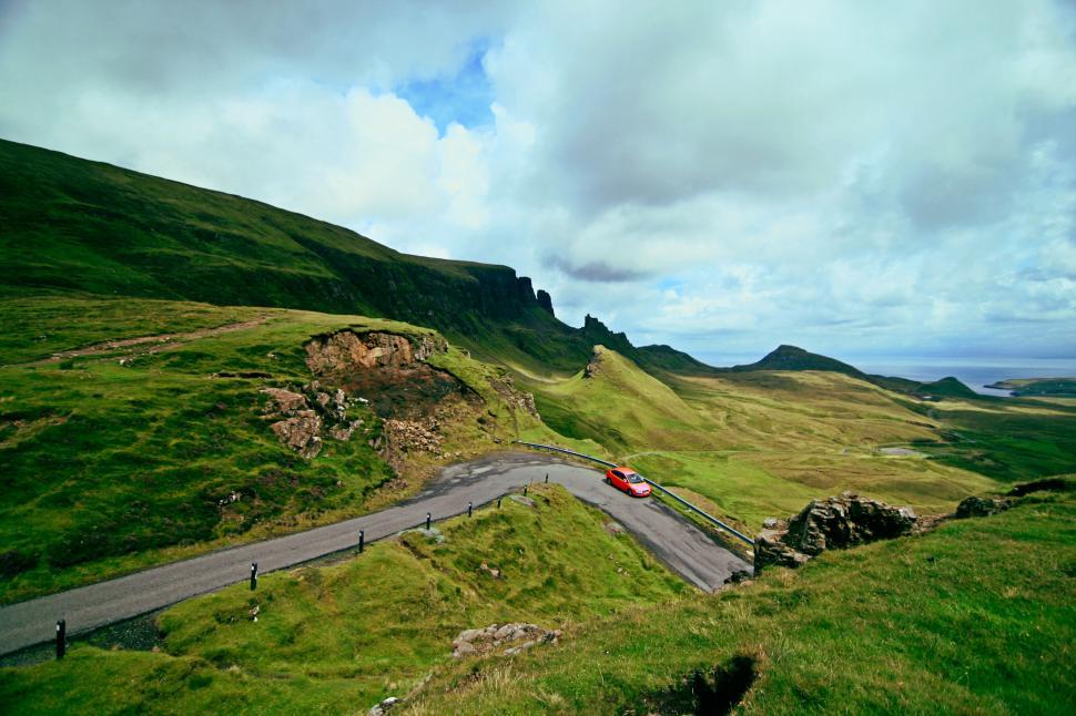 Free Image of Red car on a winding road in a vast green landscape. 
