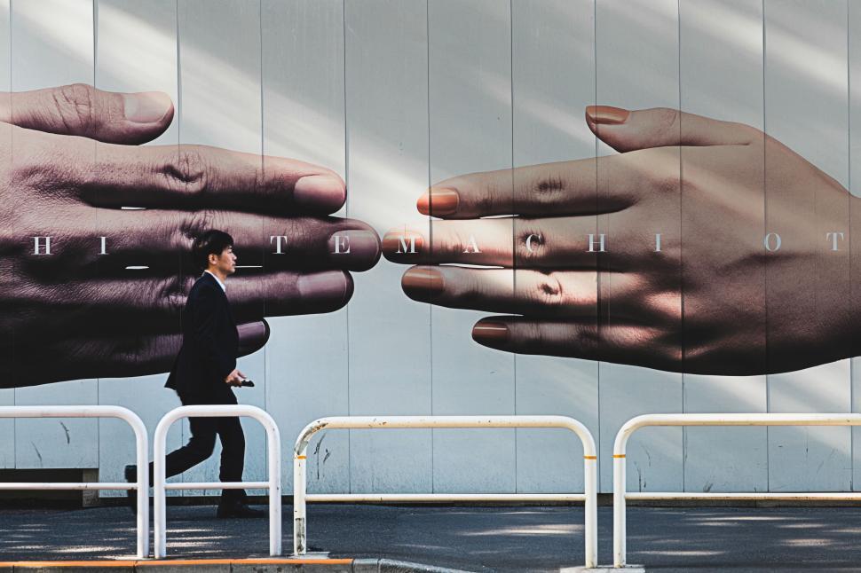 Free Image of Large hand mural with man walking on urban street 