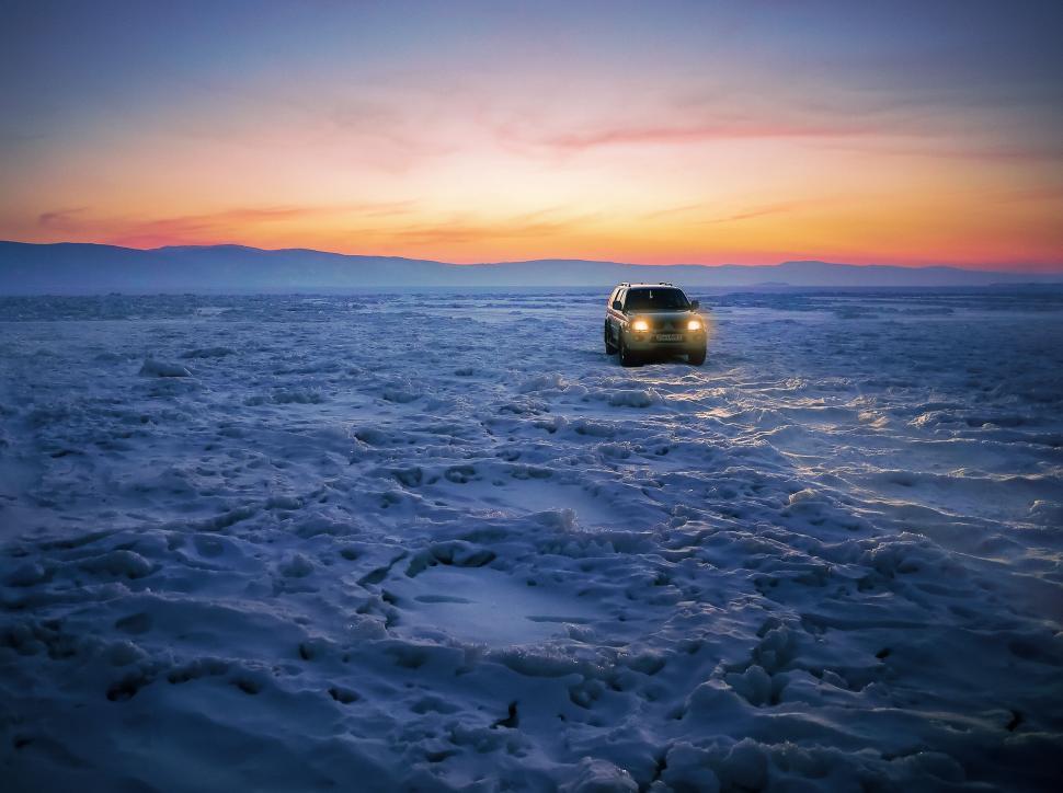 Free Image of SUV driving on a frozen lake during a golden sunset. 