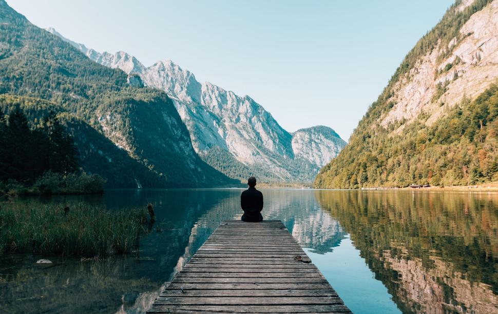 Free Image of Person seated on dock, contemplating tranquil mountain lake. 