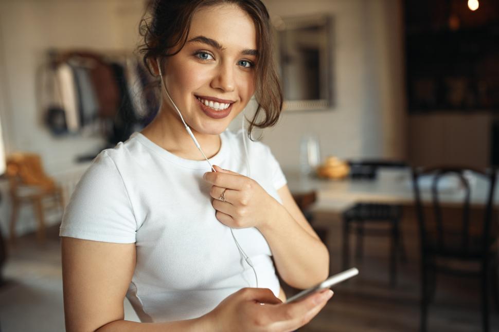 Free Image of Headshot of beautiful teen girl with chubby cheeks and curvy body posing in living room using wireless internet connection communicating online via audio chat using cell phone and earphones 
