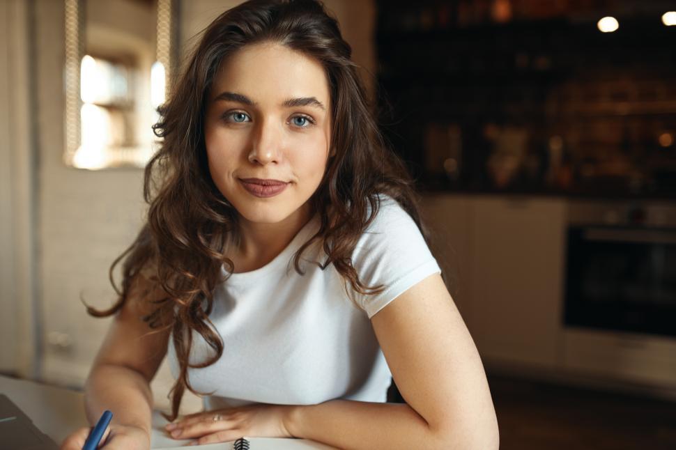 Free Image of Close up image of creative young woman copywriter making notes, planning tasks working from home using laptop. Beautiful student girl handwriting in notebook, studying distantly, preparing for test 