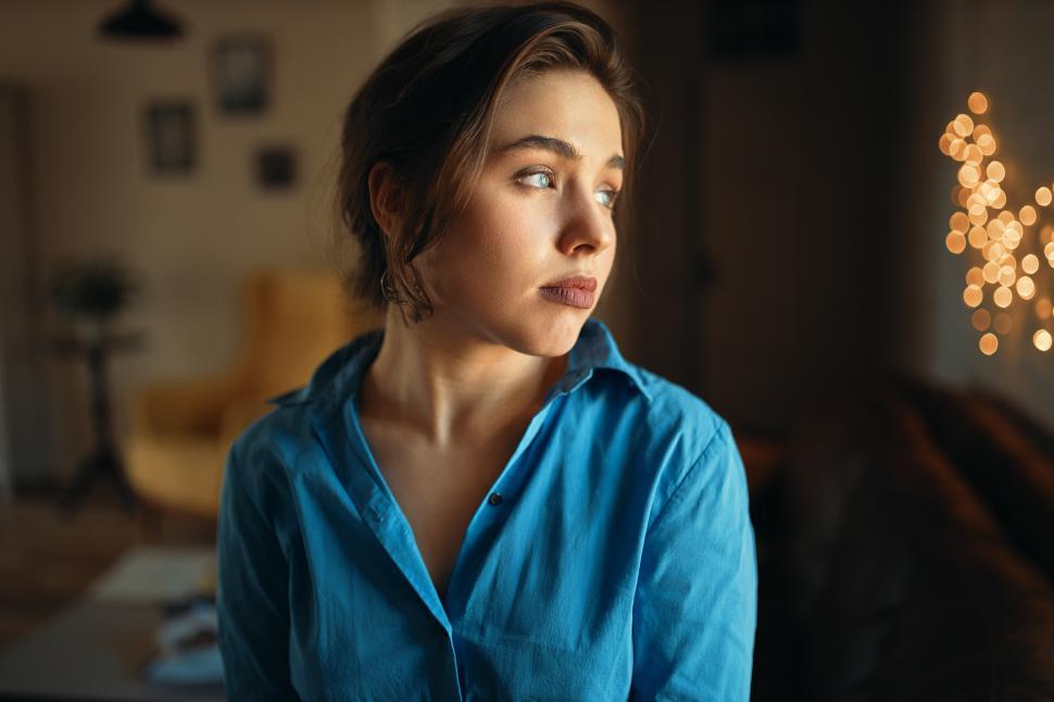 Free Image of Close up image of sad student girl in blue shirt looking away with unhappy facial expression, being bored as she has to stay at home and prepare for exam. Beautiful young female posing indoors 