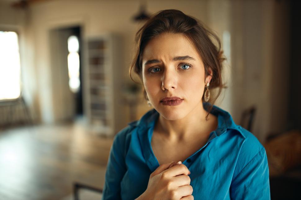 Free Image of Unhappy attractive young woman in blue shirt having mournful sorry facial expression, worrying about her future, going to cry. Upset sad girl feeling lonely, spending time at home all alone 