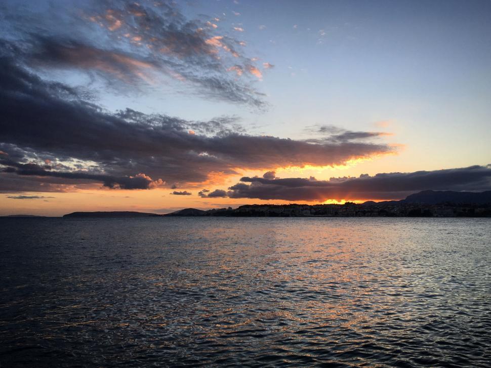 Free Image of Sunset over a calm sea with clouds and distant land view. 