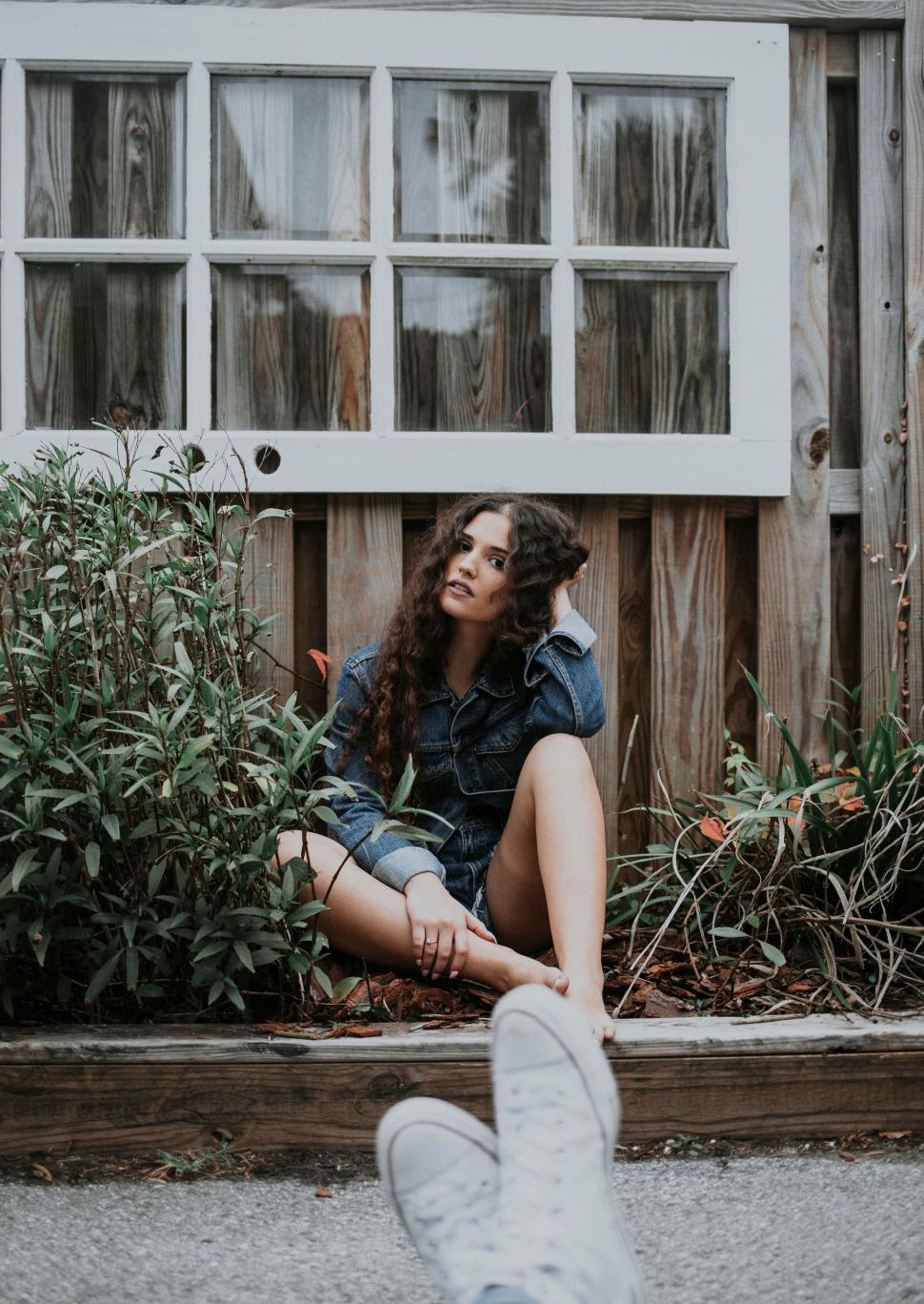 Free Image of Young woman sitting contemplatively by a wooden wall. 