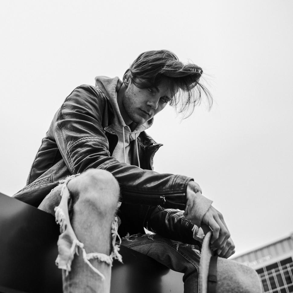Free Image of Person sitting on ledge in urban setting, black and white 