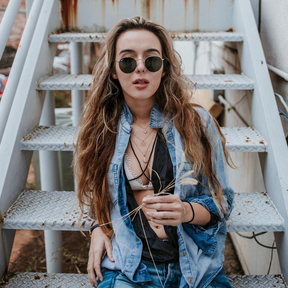 Free Image of Stylish woman holding grass while seated on metal stairs. 