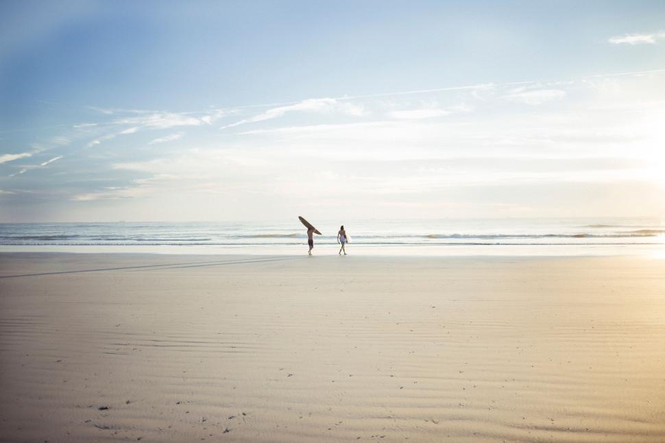 Free Image of Two people walking on a beach holding surfboards. 