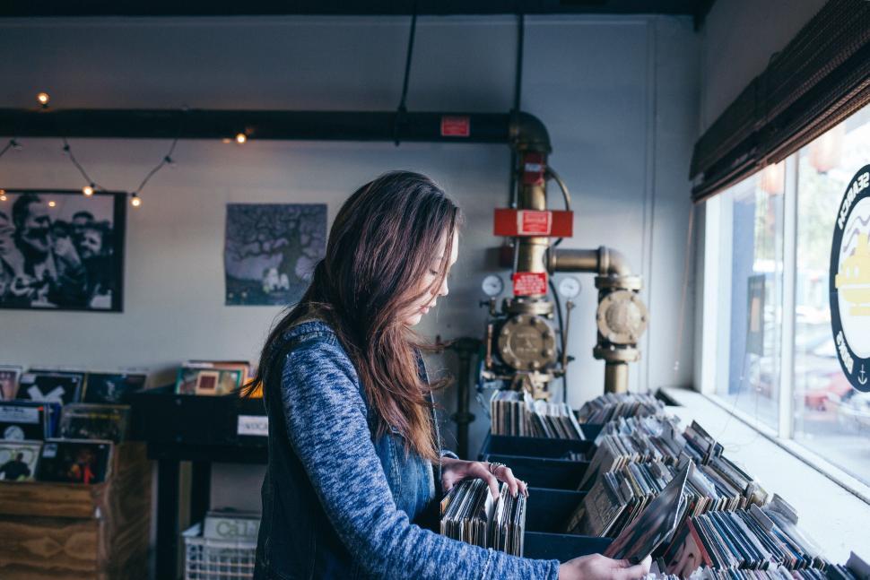 Free Image of Woman browsing records in a cozy, quaint record store. 