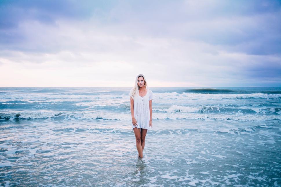 Free Image of Young woman standing on a serene beach with calm waves. 