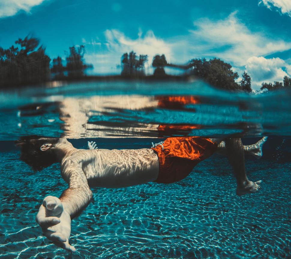 Free Image of Man floating effortlessly underwater in clear blue pool 