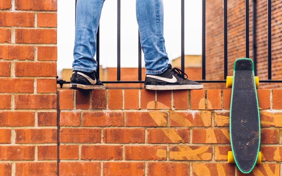 Free Image of Person standing on brick wall next to leaning skateboard. 
