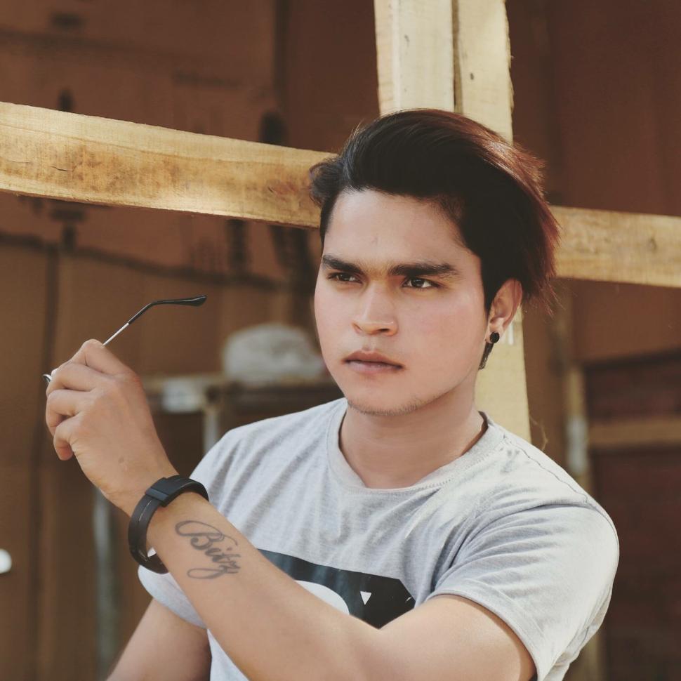 Free Image of Young man with tattoo holding sunglasses outdoor scene 