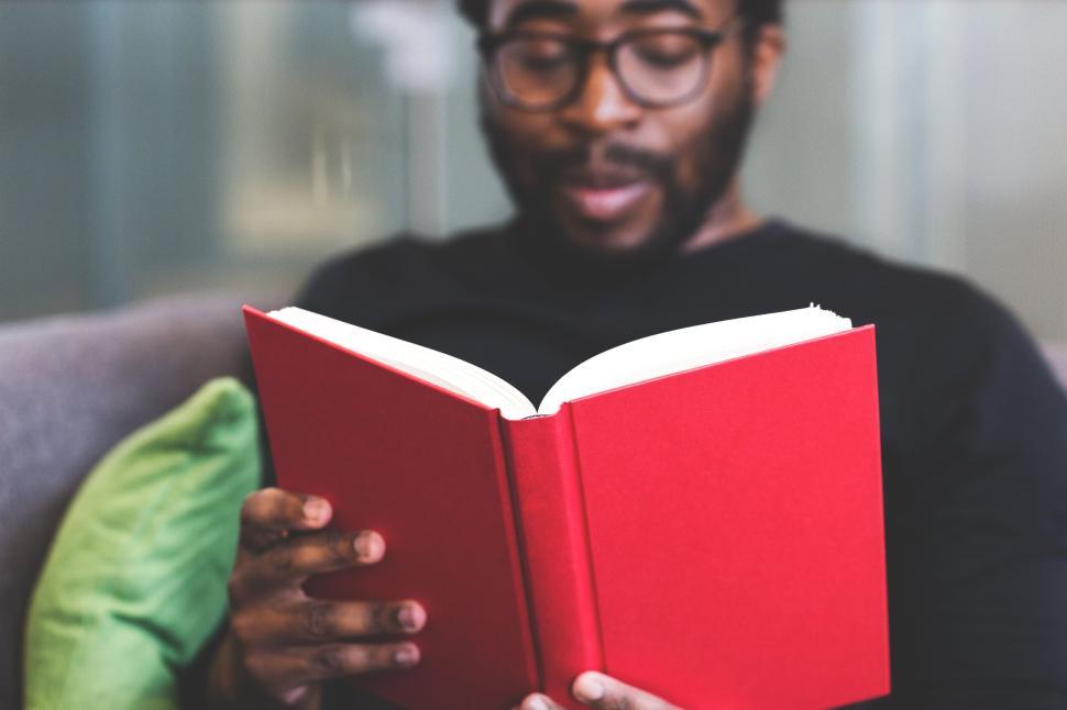 Free Image of Man reading a red book indoors with a relaxed ambiance 