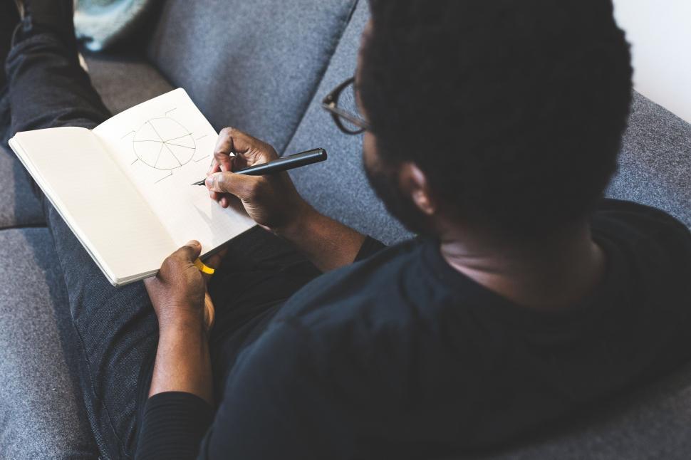 Free Image of Person drawing a diagram in notebook while relaxing on sofa. 