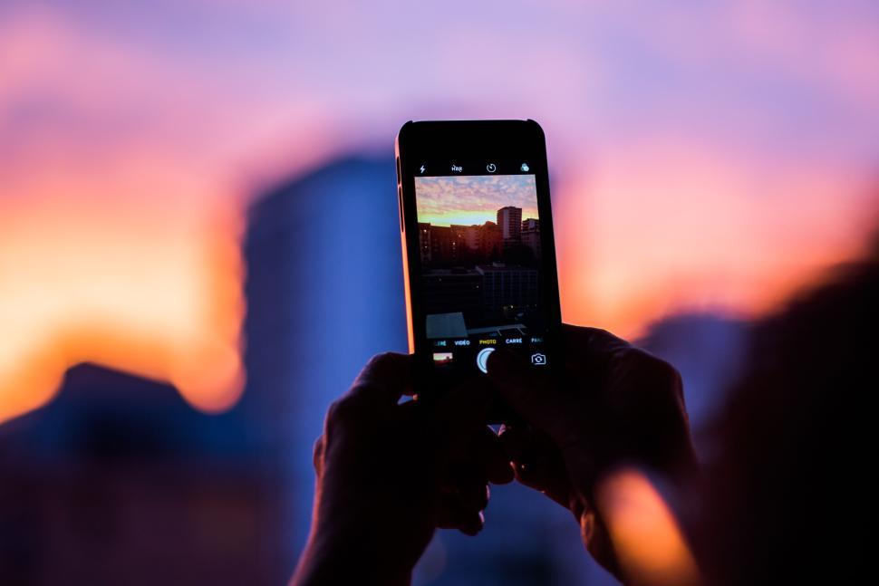 Free Image of Hands holding phone capturing a cityscape at sunset. 
