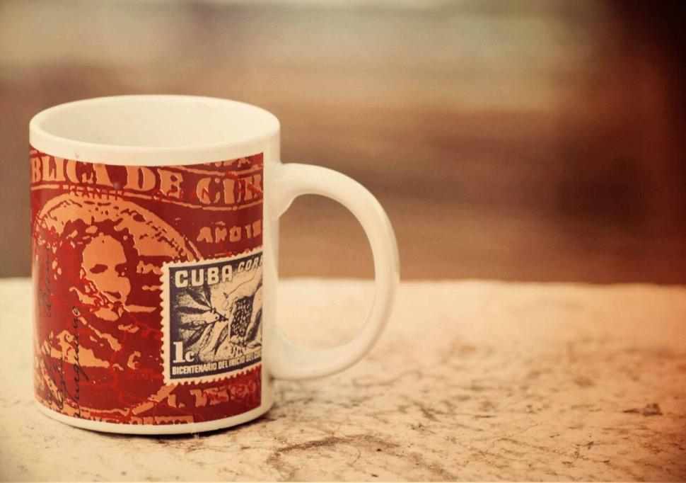Free Image of Vintage-style cup with Cuban stamp art on rustic surface 