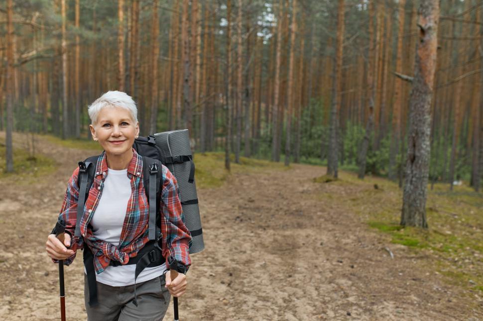 Free Image of Leisure, hobby and outdoor activities concept. Energetic blonde female pensioner enjoying beautiful wild nature, using sticks for nordic walking, spending summer weekend away from city noises 