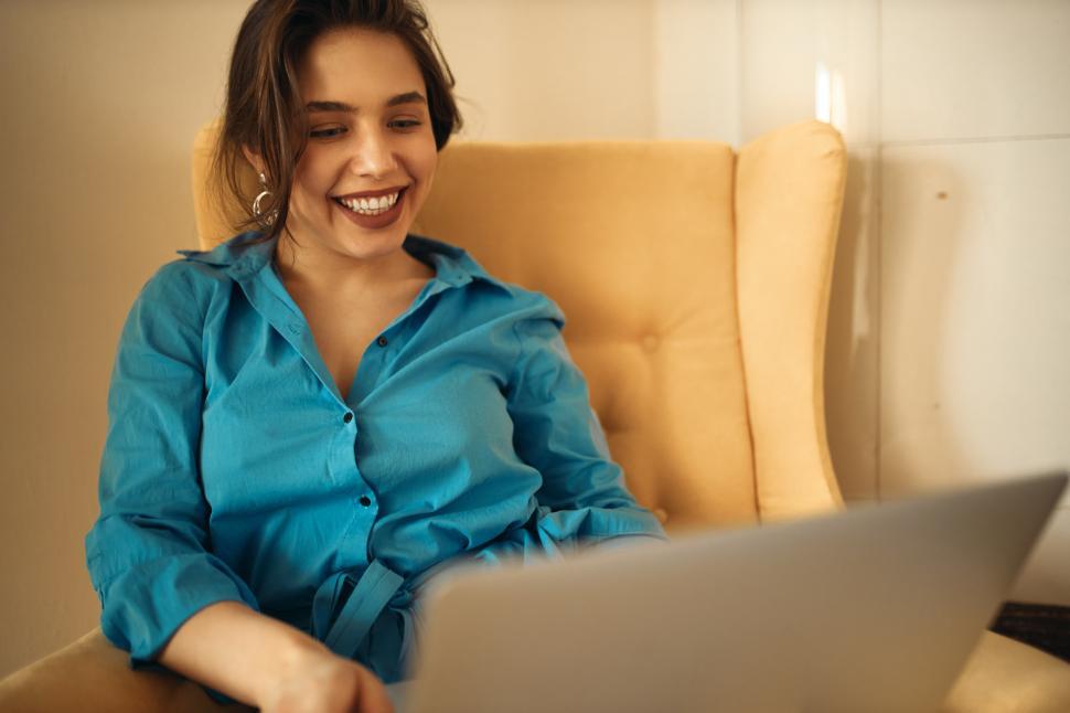 Free Image of Portrait of cheerful teenage girl sitting in armchair with laptop, smiling broadly, enjoying online communication, speaking to friends via video conference group call, sharing news, having fun 