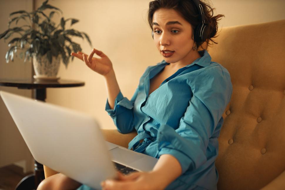 Free Image of Stylish confident young woman headphones sitting on sofa with laptop participating in group business online meeting using webcam conference chat, gesturing emotionally, brainstorming with colleagues 