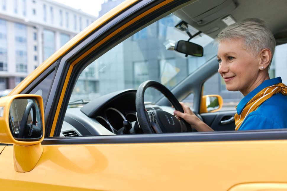 Free Image of Beautiful mature female with pixie hair driving car, enjoying empty streets early in the morning. Attractive middle aged woman sitting in driver s seat, parking automobile, looking at side view mirror 