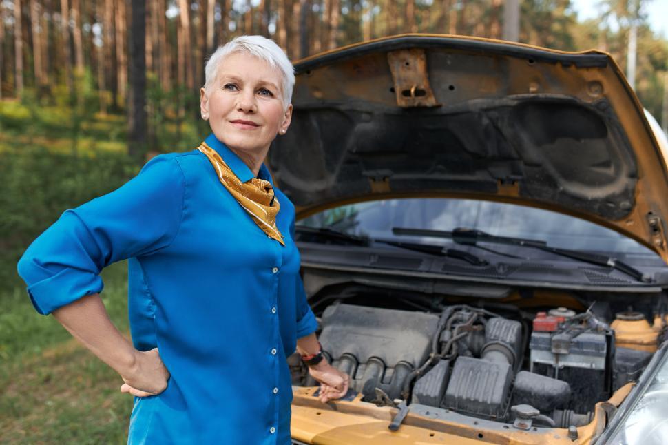 Free Image of Portrait of mature female with blonde short hair having frustrated facial expression because car in broken. Stressed middle aged woman waiting for service after vehicle breakdown, opening hood 