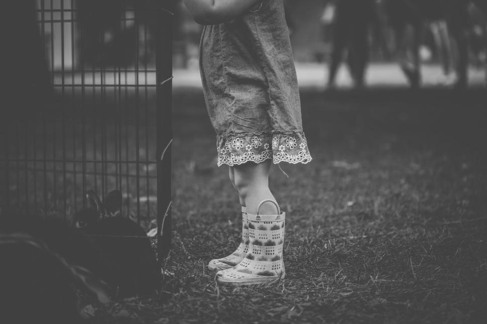 Free Image of Small child in rain boots standing at a fence s edge 