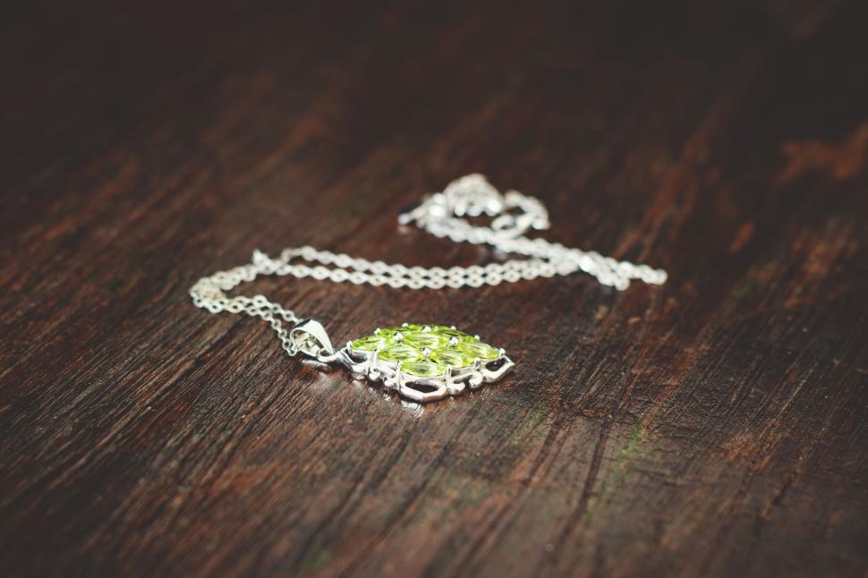 Free Image of Ornate silver necklace with green gemstone on wood 