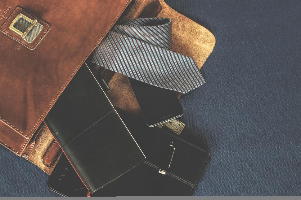 Free Image of Leather bag with tie, notebook, and phone spilling out 