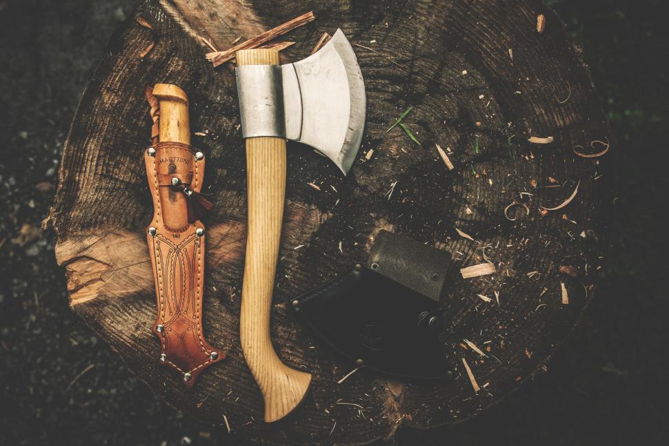 Free Image of A rugged axe with sheath and leather knife on a stump. 
