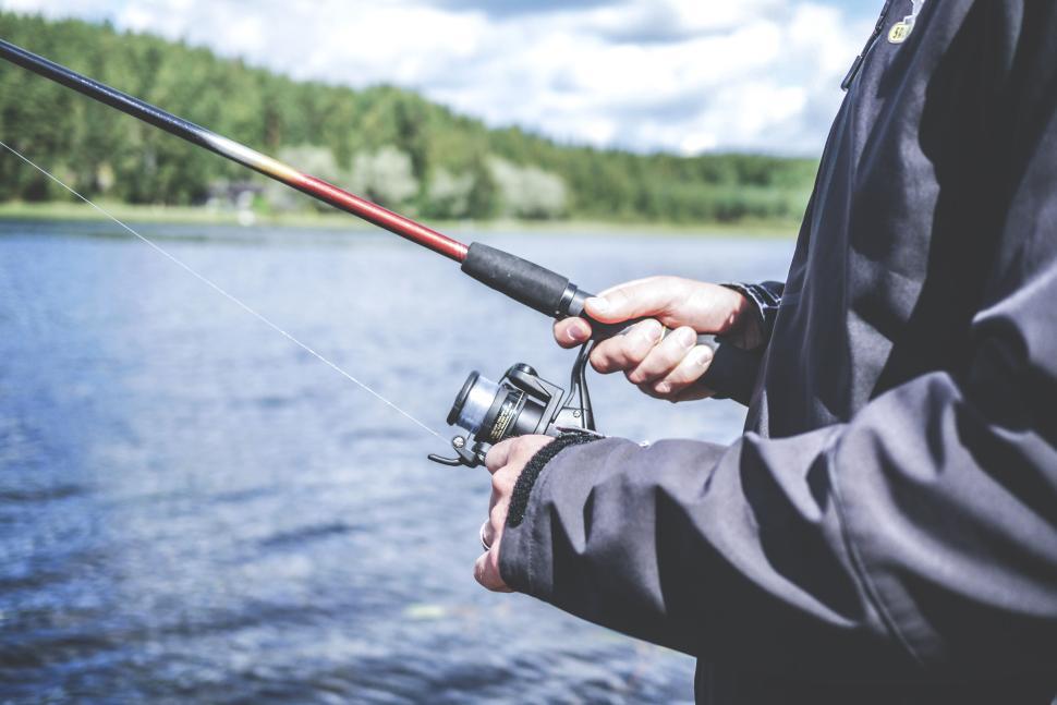Free Image of Man holding fishing rod while standing by a lake 