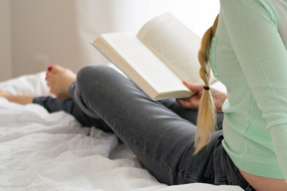 Free Image of Person on bed reading a book with focus on the book. 