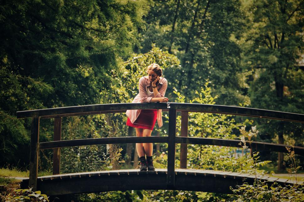 Free Image of Woman standing on wooden bridge in lush green forest 