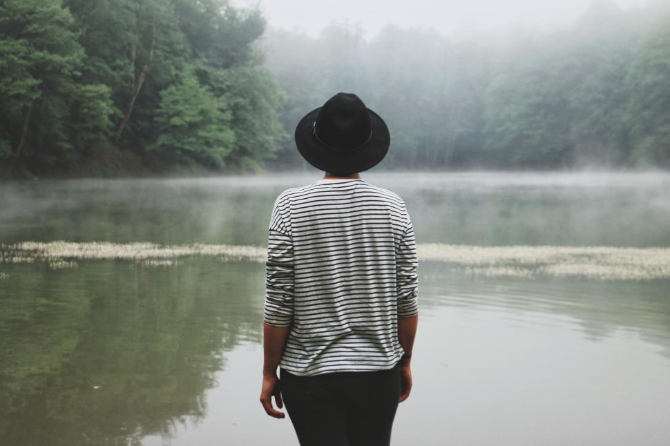 Free Image of Person by misty forest lake, wearing a black hat, stripes. 