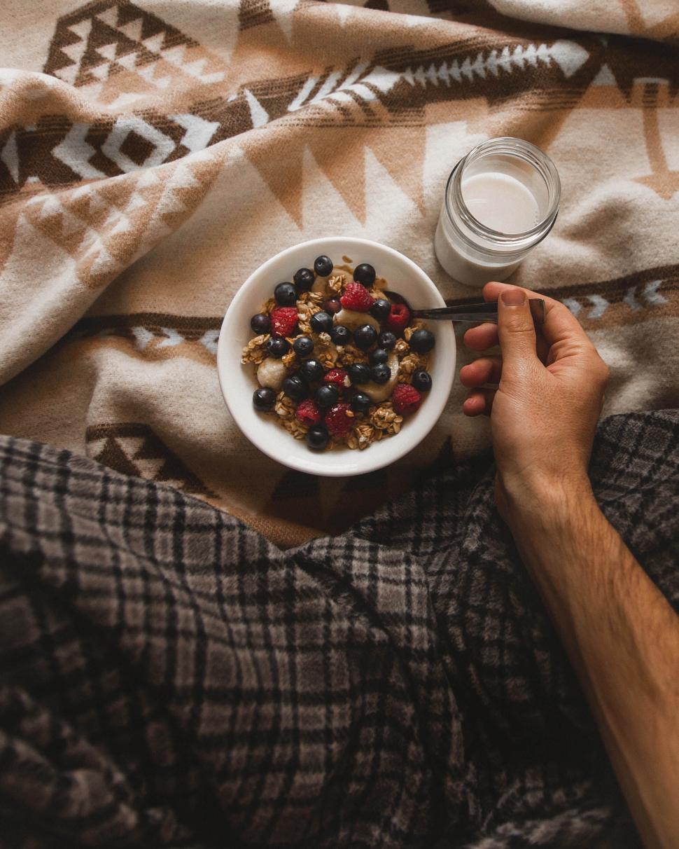 Free Image of Hand holding bowl of fruit and granola on blanket 