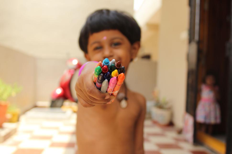 Free Image of Smiling child holding colorful crayons towards the camera 
