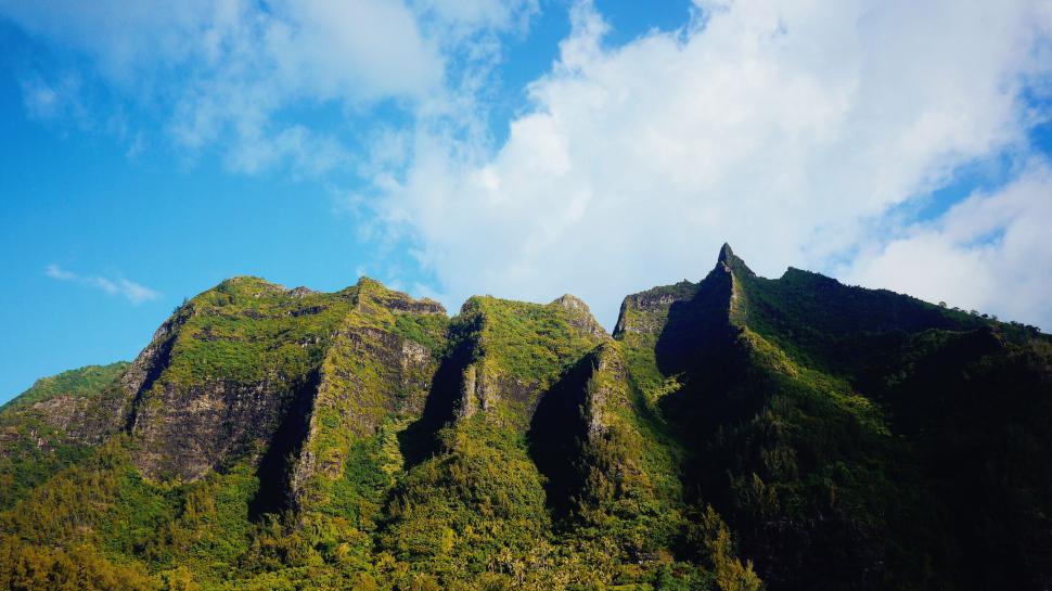 Free Image of Green mountains under a bright blue sky with clouds. 