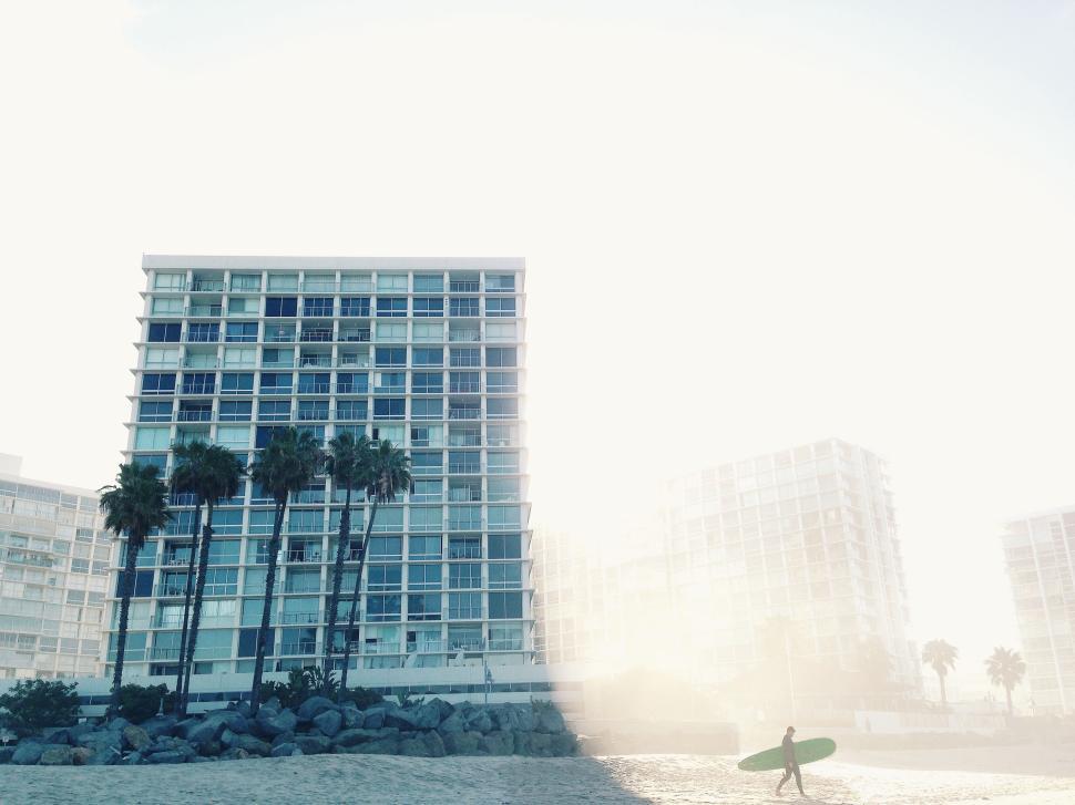 Free Image of Modern beachfront buildings with a lone surfer. 