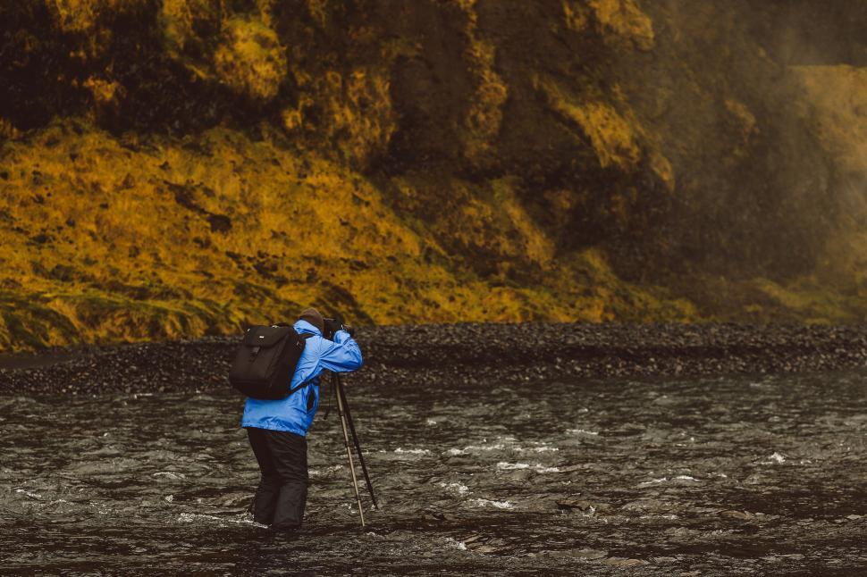 Free Image of Photographer standing on rocky shore with a tripod. 