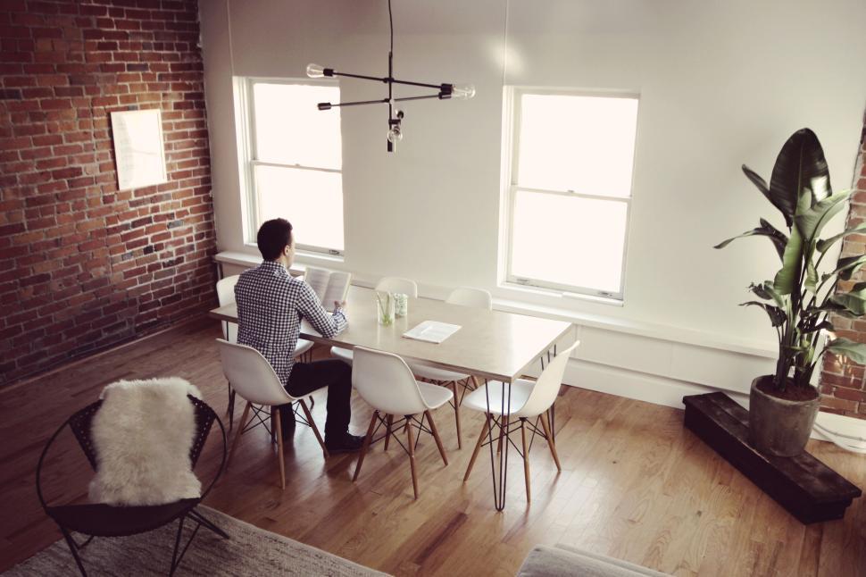 Free Image of Person reading at sunny table in brick-wall room. 