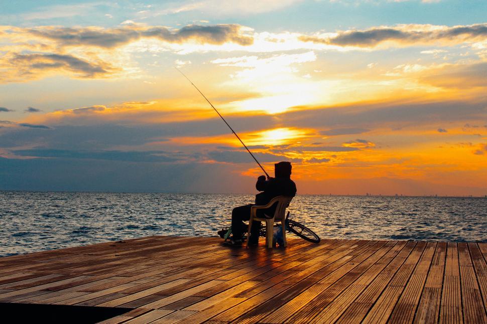 Free Image of Person fishing alone at a pier during a sunset, peaceful. 