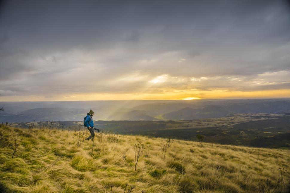 Free Image of Person hiking on grassy terrain under cloudy sky 