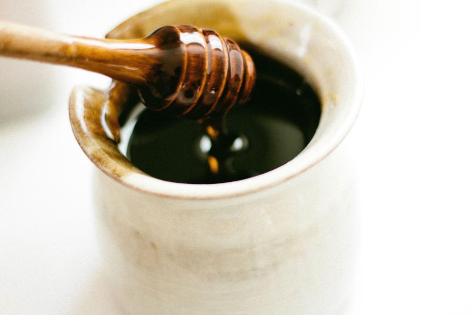Free Image of Close-up of honey drizzling from dipper into white jar 