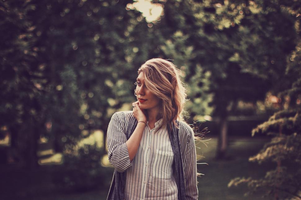 Free Image of Woman in garden, striped shirt, touching face gently. 