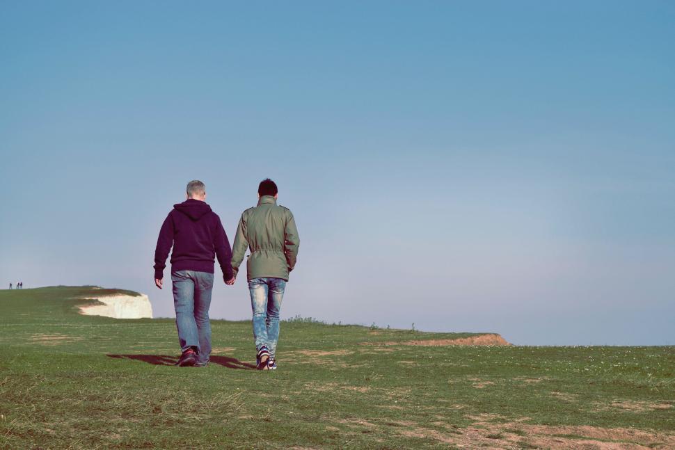 Free Image of Two people holding hands walking on a grassy field. 