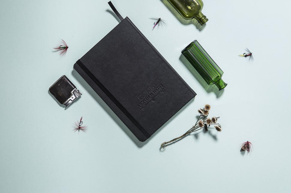 Free Image of Black notebook with green bottles and dry flowers on table 