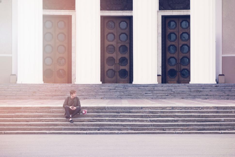 Free Image of Person resting on steps of grand building with columns 