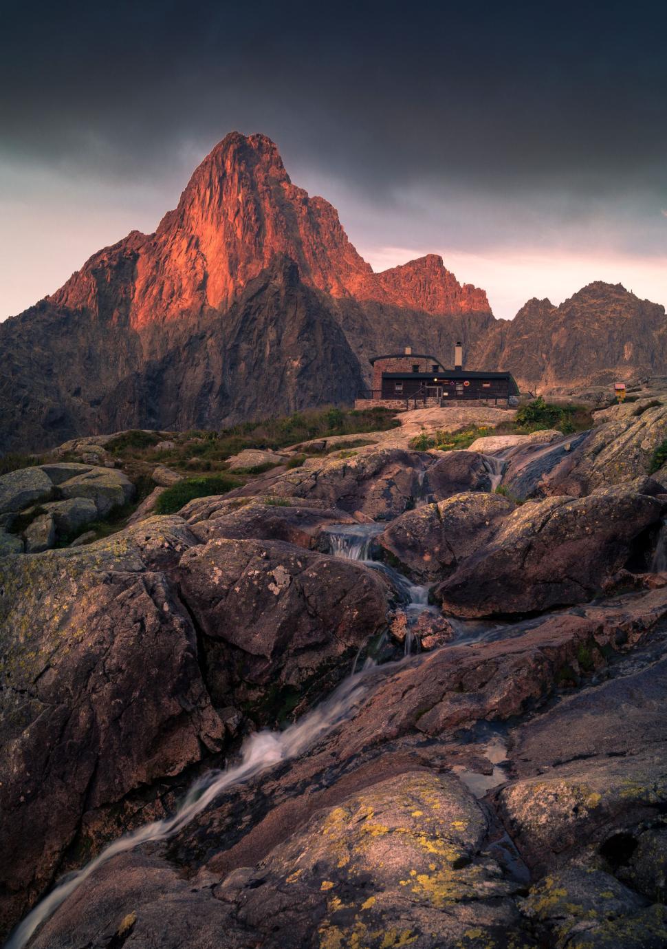 Free Image of Sunset illuminating mountain peak with cabin nearby 